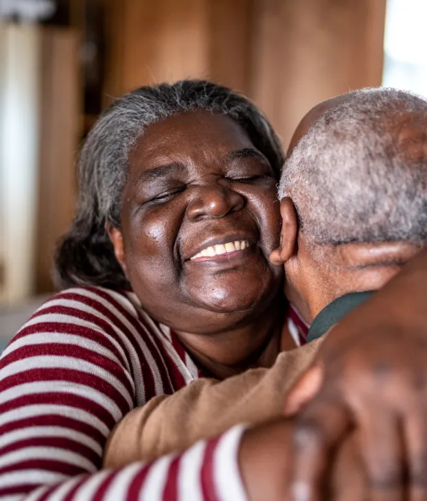 elderly pair hugging with woman facing the camera and smiling over his shoulder