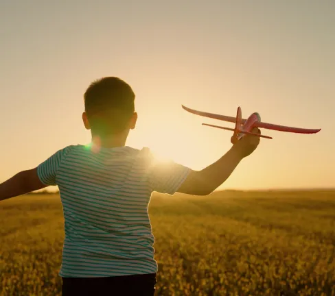 boy facing the sunset playing with a toy plane